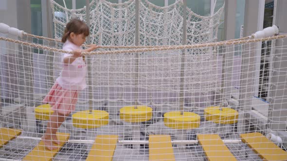 Toddler girl hopping along bouncing bridge in play area, showing ...
