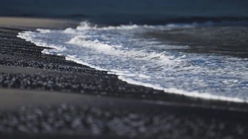 Slowly waves roll on the sandy shore. Blurred silhouettes of a human and a dog in the background. Sl