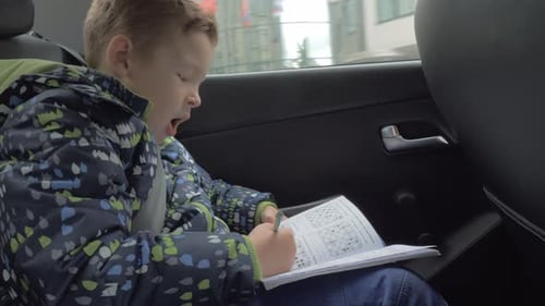 Boy Concentrating on Homework in the Back Seat of Car