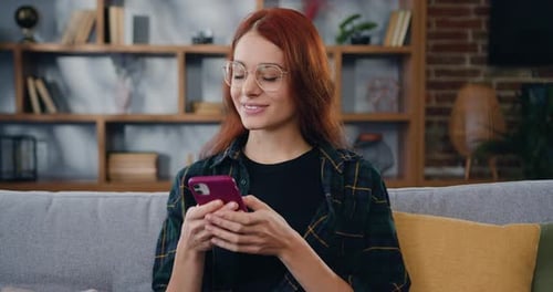 Woman Smiles Using Smartphone on Couch at Home