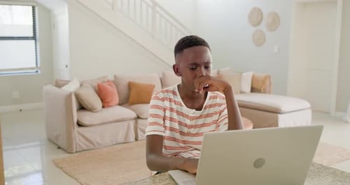 Male youth sitting at counter, studying on laptop, facing issue, pausing then relaxing into smile