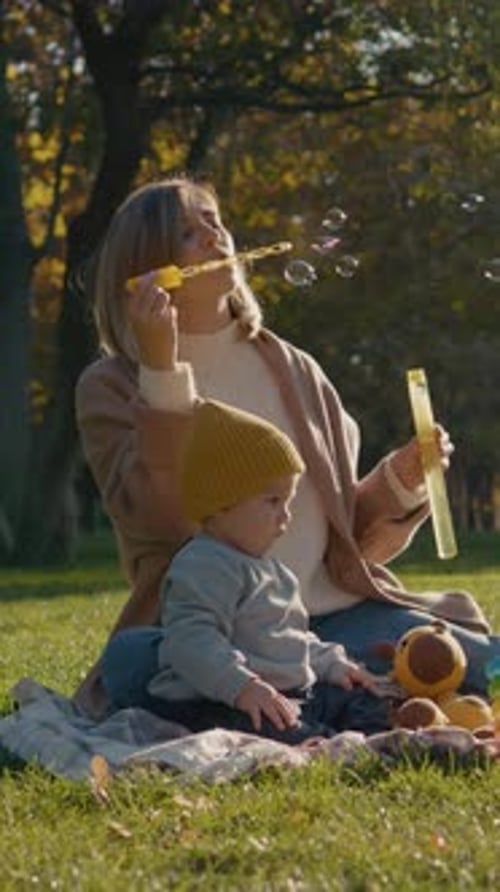 Vertical video Mother and child blowing soap bubbles in a park