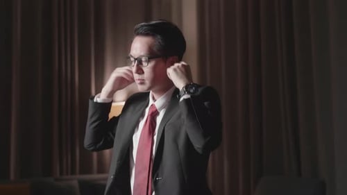 Man in Suit Adjusts Tie and Puts on Glasses