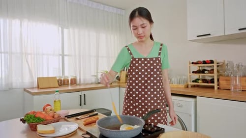 Woman Cooking Egg and Sausage in Bright Kitchen
