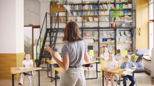 A Modern Young Elementary School Teacher is Conducting a Lesson Standing with Her Back to the Camera