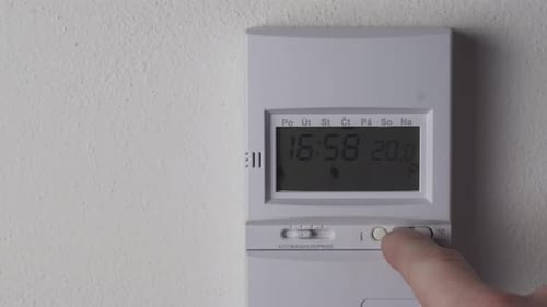 Lowering heating thermostat temperature, display and hand closeup view, reducing costs