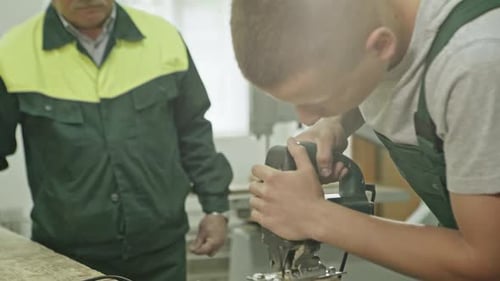Young Man Using Jigsaw in Workshop With Senior