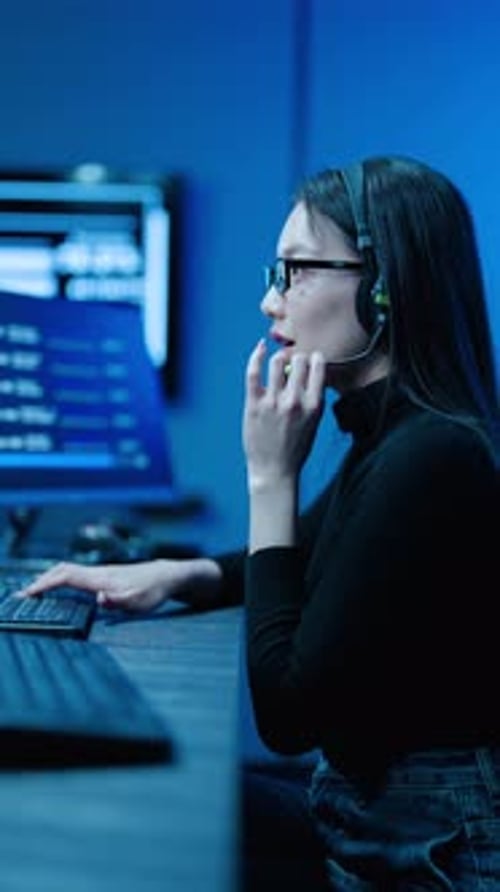 Une femme asiatique spécialiste du support informatique portant un casque et des lunettes surveille les données sur plusieurs ordinateurs