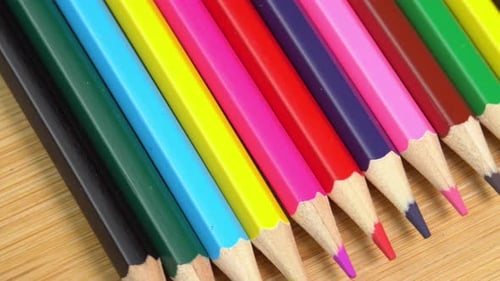 Dolly shot of vibrant coloured pencils on wooden desk