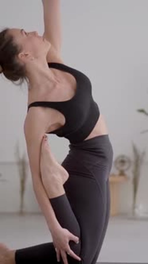 Vue latérale : jeune femme caucasienne en vêtements de sport gris faisant du yoga, posture à une jambe, posture du roi pigeon