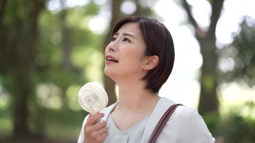Woman Fanning Herself in the Park on Sunny Day