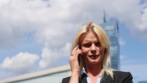 Young businesswoman talking on the phone while standing outside in the street under office buildings