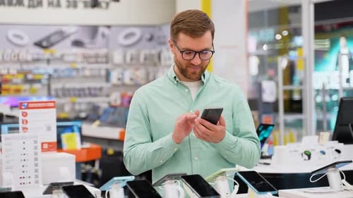 Happy Young Man Choosing a New Smartphone in a Tech Store