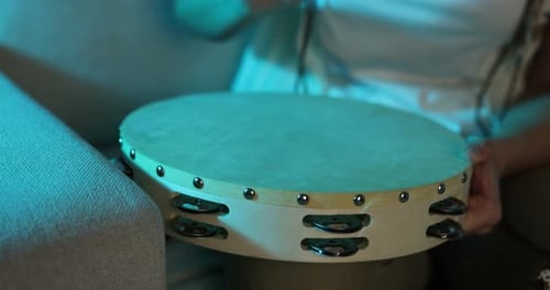 Woman playing tambourine in color light at home, closeup