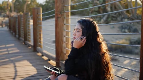A slow motion shot of a beautiful girl in the desert at sunset reading text messages and using socia