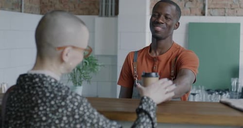 Joyful Barista Giving to Go Coffee to Cheerful Young Woman Customer Smiling in Cafe at Counter