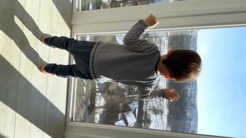 Adorable little baby boy stands near the window on sunny day.