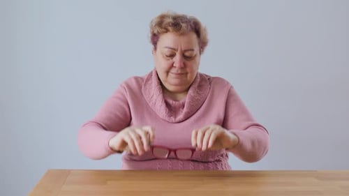 Adult Takes off Reading Glasses and Sits at Table