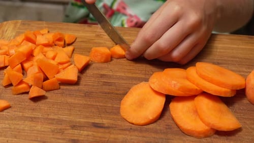 Dicing orange carrots on a wooden cutting board