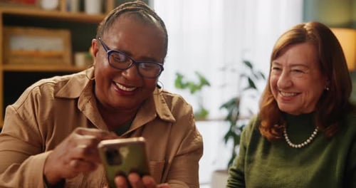 Women Laughing while Looking at Phone Indoors