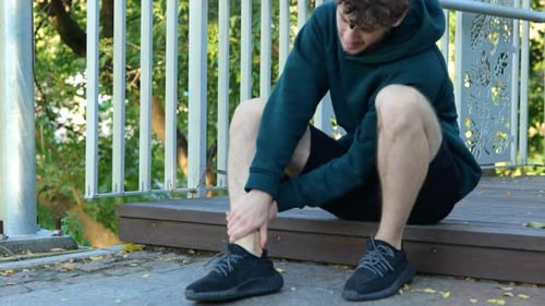 Young Caucasian Man Sitting on Stairs Leg Hurts Man Massaging His Feet Outdoor Activities Sportsman