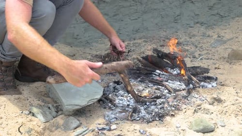 A close up of a man cooking a fish bush style on hot coals on a fire on the coastline.