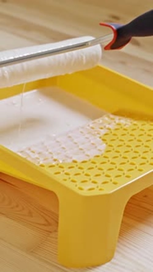 Paint roller dipped in white paint on yellow tray during home renovation