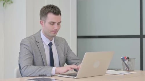 Young Businessman Celebrating Online Success on Laptop in Office