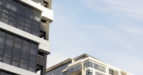 Camera tilting upward, revealing high-rise facade climbing past balconies against pale blue sky