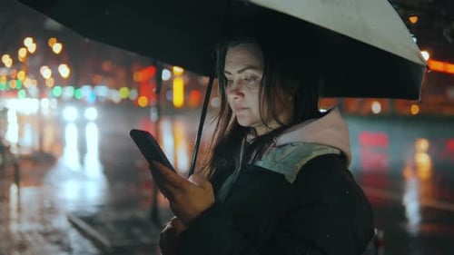 Woman with Smartphone in City Rain at Night