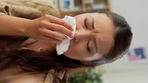 Woman with a cold wiping her nose at home