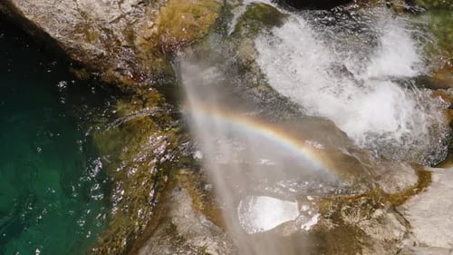 A Waterfall Cascading Over Rocks Into A Pool, Creating A Mist. A Rainbow Forms Within The Mist.