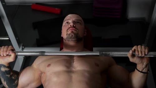 Gros plan d'un homme musclé faisant un développé couché allongé sur un banc dans une salle de sport sombre