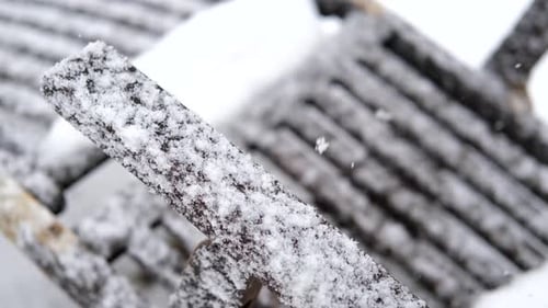 close up of snowflakes falling on the handle of a wooden sun lounger