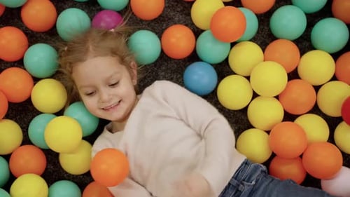 Une petite fille mignonne heureuse jouant avec des boules de couleur dans la piscine à balles de l'aire de jeux et profitant du week-end à