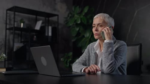 Woman Talks on Phone While Using Laptop in Office