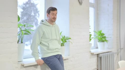 Man Leans Contemplatively on Windowsill During Snowfall