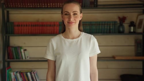 Portrait of a Confident Happy Attractive Student Standing Against the Background of Bookshelves in