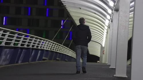 Mature adult crossing city pedestrian bridge location, nighttime scene