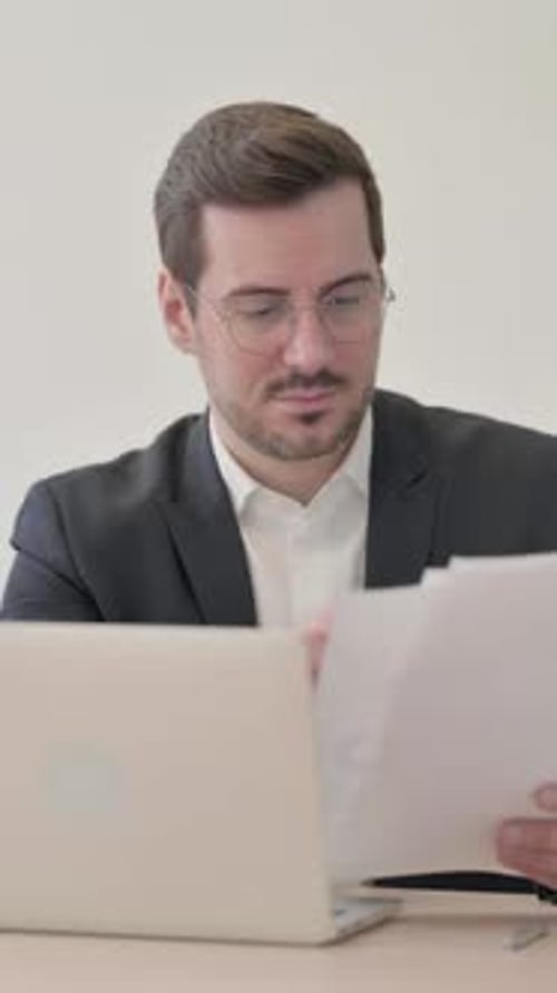 Man in Suit Reviews Documents at Desk with Laptop