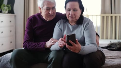 Loving Senior Couple Using Smartphone on Bed