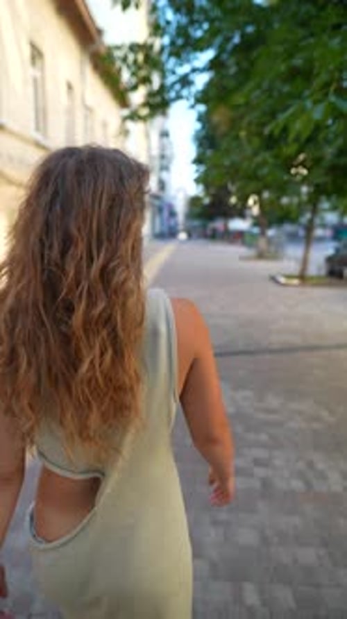 Amidst the Golden Evening Sunlight a Beautiful Girl with Red Curly Hair Wanders Through the City