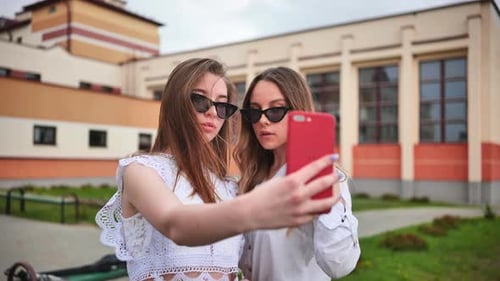 Two Girls Schoolgirls Make a Selfie Using a Smartphone Against the Background of the School
