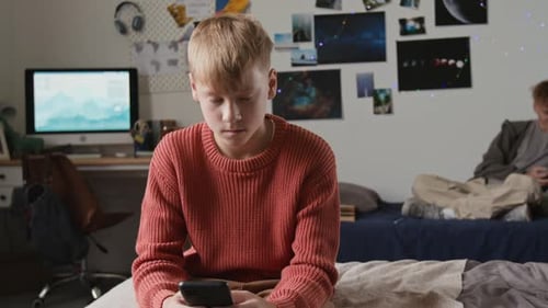 Teenager Using Phone While Friend Sits On Bed
