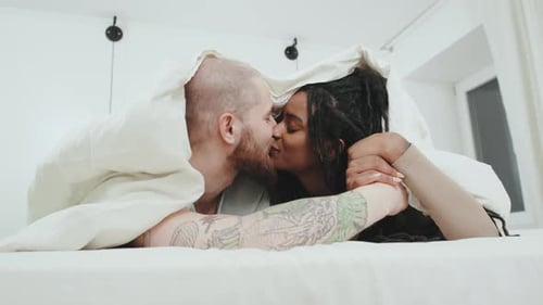 Couple Intimately Kissing Under White Sheets in Bedroom