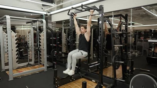 Strong athletic American man doing hanging knee raises, working out on horizontal bar in a fitness