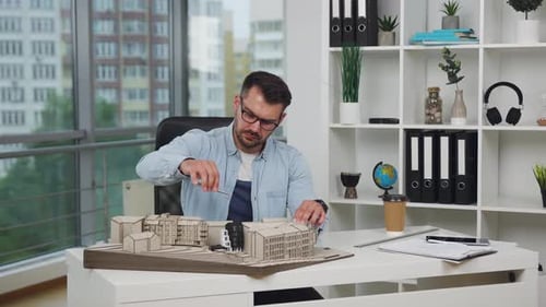Man architect in glasses which working with wooden construction of future buildings in design office
