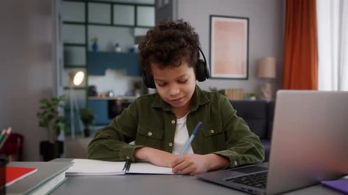 Boy Writing in Notebook Studying with Laptop
