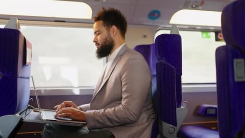 Ein Geschäftsmann, der während einer Bahnfahrt an seinem Laptop arbeitet und moderne Konnektivität hervorhebt