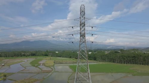 Helix drone shot of high voltage electric tower build on the middle of rice field plantation. Electr